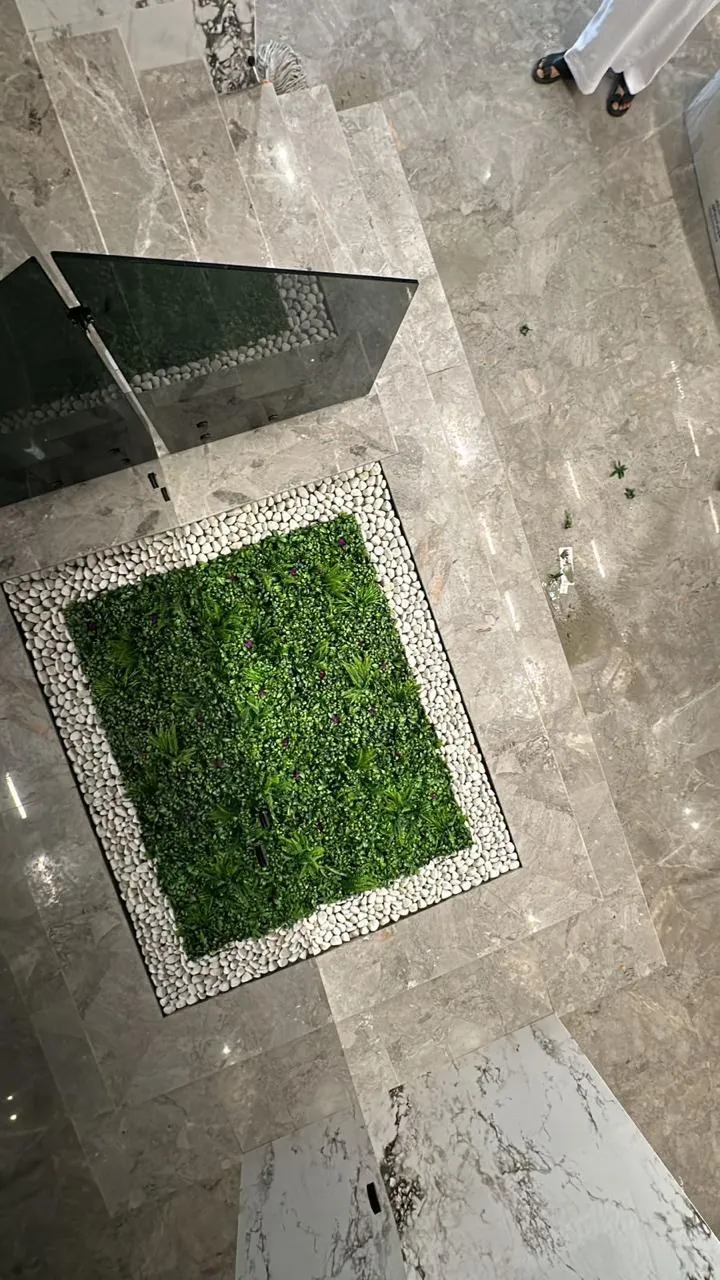 منظر علوي لحوض عشب صناعي مربع محاط بحصى أبيض على أرضية رخام رمادي